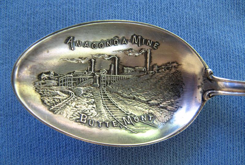 Souvenir Mining Spoon Bowl Anaconda Mine.JPG - SOUVENIR MINING SPOON ANACONDA MINE BUTTE MT - Sterling silver spoon embossed with a detailed picture of the Anaconda Mine in bowl, markedANACONDA MINE BUTTE, MONT, with full handled birds-eye view of the Hill with dozens of mines and head-frames in detail, reverse marked THE RICHEST HILL ON EARTH and Sterling with maker’s mark for Paye and Baker of North Attleboro, MAwho made silver spoons from 1901-c1930, length 4 3/8 in. [The Anaconda Copper Mine was the largest copper-producing mine in the world from 1892 through 1903.  Located in Butte, Montana it transformed this small and poor town into one of the most prosperous cities in the country, often called the Richest Hill on Earth.  This small silver mine was bought in 1881 by Marcus Daly from Michael Hickey. Hickey was a prospector and Union Civil War veteran, and named his claim the Anaconda Mine after reading Horace Greeley's Civil War account of how Ulysses S. Grant's forces had surrounded Robert E. Lee's forces "like an anaconda". Daly then developed the Anaconda Mine in partnership with George Hearst, father of William Randolph Hearst, and James Ben Ali Haggin and Lloyd Tevis of San Francisco.  Huge deposits of another mineral, copper, were soon discovered.  Daly quietly bought up neighboring mines forming a mining company and would eventually own all the mines on Butte Hill. He then built a smelter at Anaconda which he connected to Butte by a railway. From this beginning grew the Anaconda Copper Mining Company, a global mining enterprise featuring the Anaconda and other Butte mines, a smelter at Anaconda, Montana, processing plants in Great Falls, Montana, the American Brass Company, and many other properties, mostly in the United States and Chile. The Anaconda Copper Mining Company was acquired by ARCO in 1977.  The Anaconda mine itself was closed in 1947 after producing 94,900 tons of copper. Its location has been consumed by the Berkeley Pit, a vast open-pit mine.  In 1977, Anaconda was sold to the Atlantic Richfield Company (ARCO) for $700 million.  By 1983 the Berkeley Pit was completely idle and ARCO suspended all operations in Butte.]